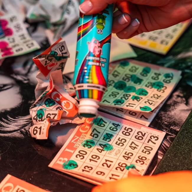 Close-up of bingo cards with green markers and torn number tabs beside a colorful bingo dauber during a game.