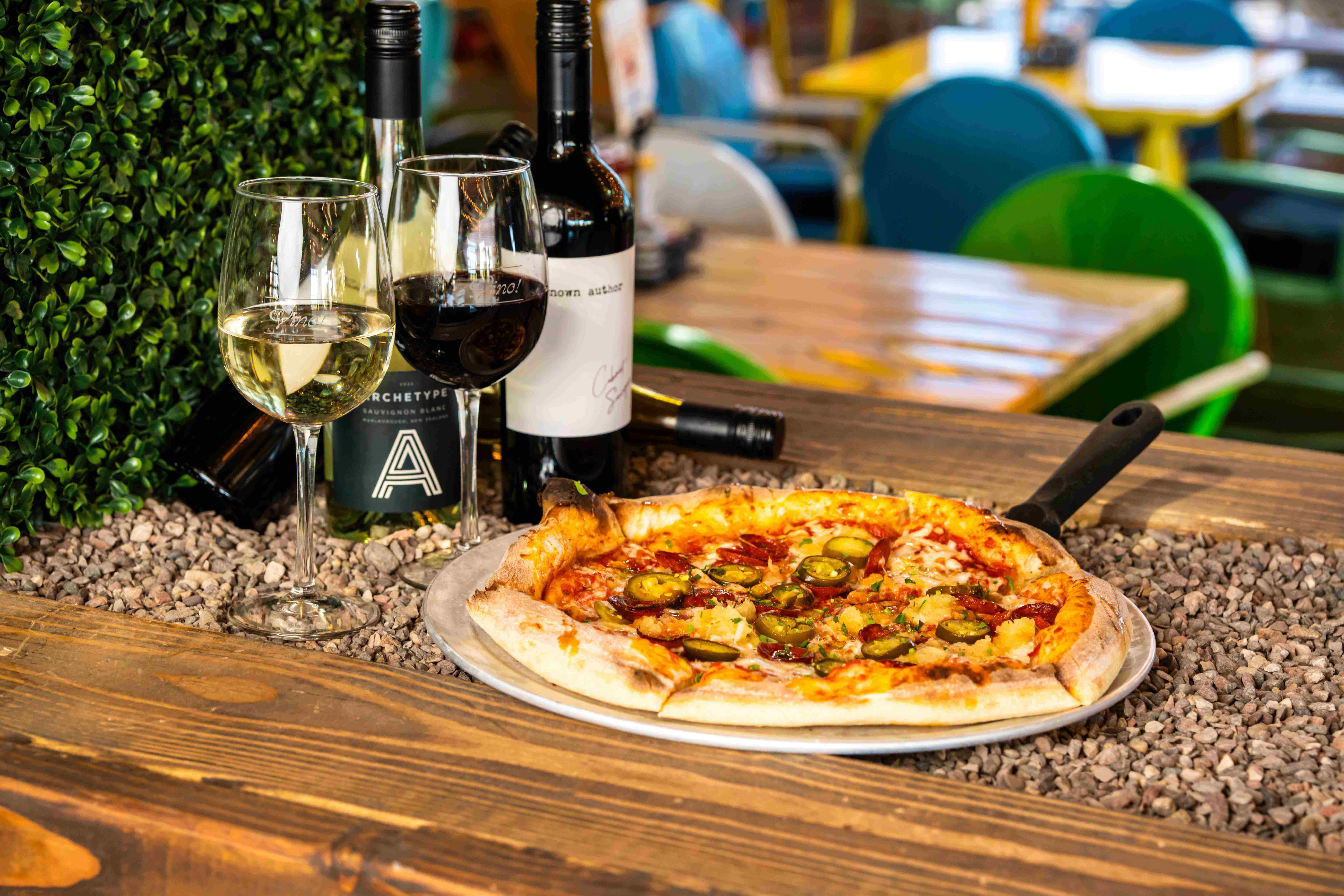 Pizza and glasses of red and white wine served on a patio table at Backyard Desert Ridge.