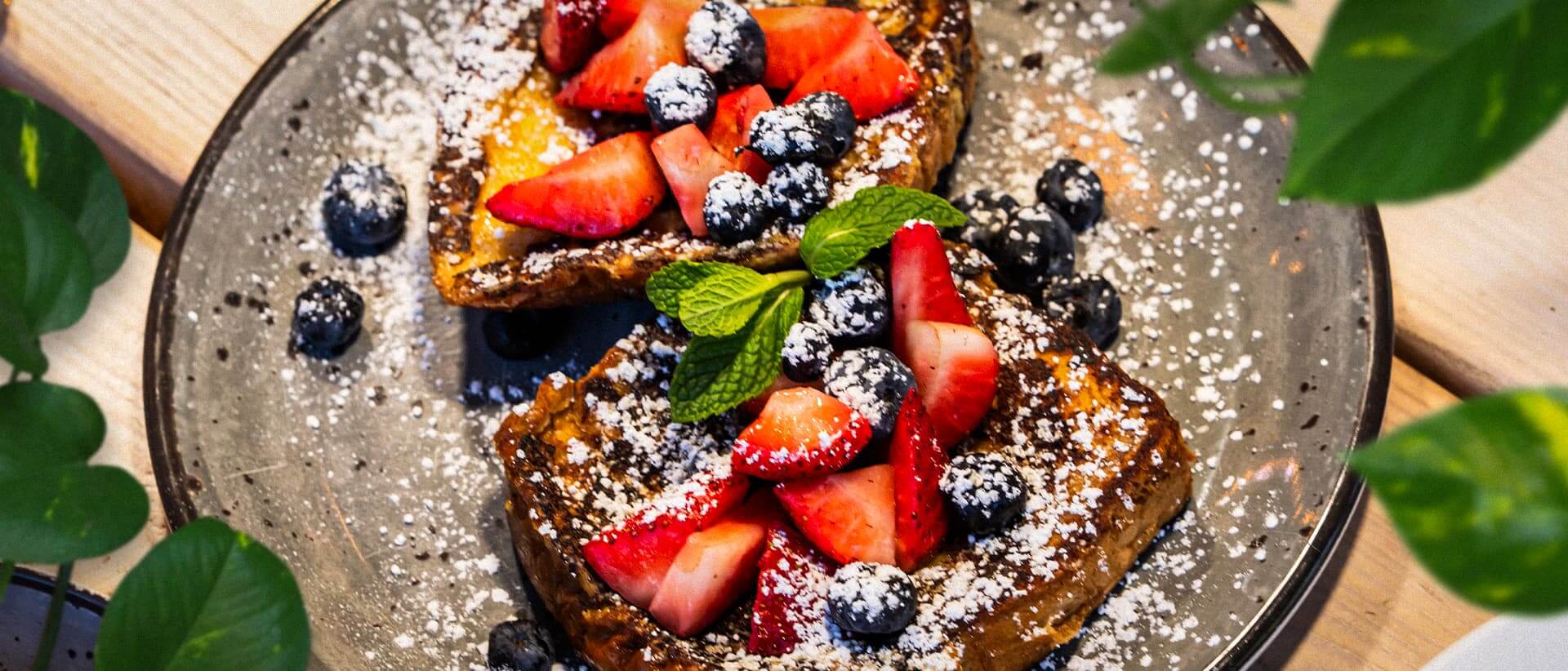 French toast topped with fresh strawberries, blueberries, powdered sugar, and mint garnish served on a rustic plate for weekend brunch.