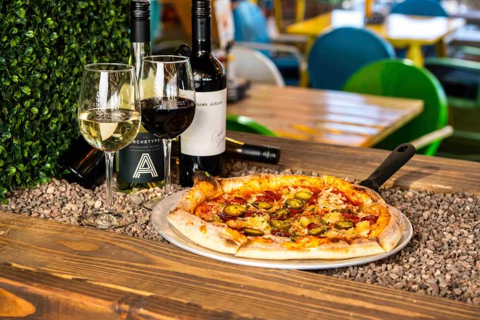 Pizza and glasses of red and white wine served on a patio table at Backyard Desert Ridge.